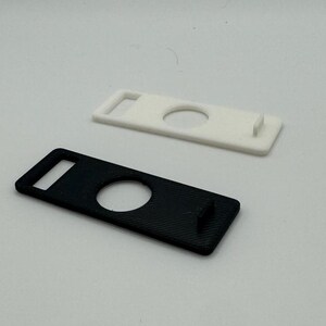 Pu&ograve; includere: Due portachiavi in plastica, uno nero e uno bianco, con un ritaglio circolare al centro. Entrambi i portachiavi hanno un piccolo anello rettangolare nella parte superiore.