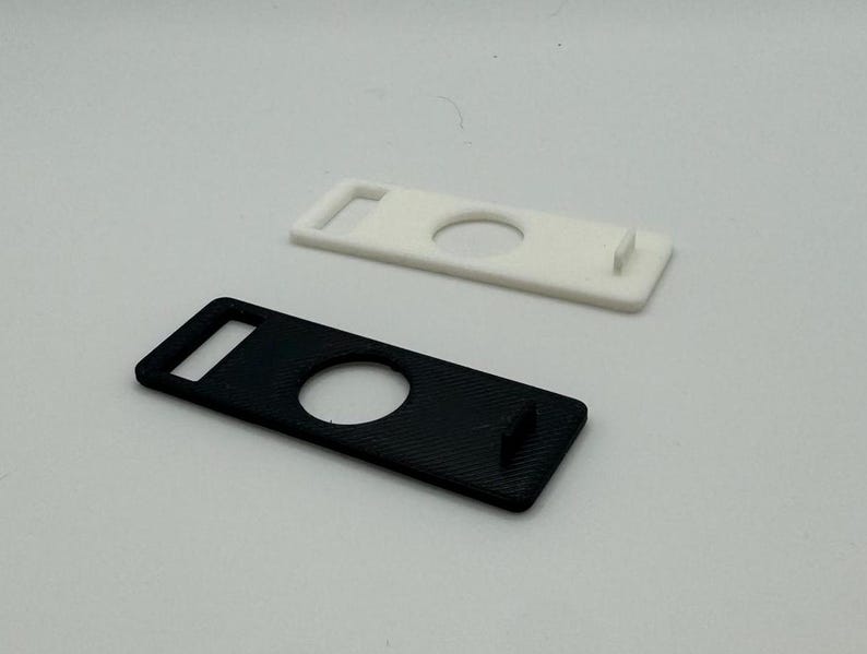 Pu&ograve; includere: Due portachiavi in plastica, uno nero e uno bianco, con un ritaglio circolare al centro. Entrambi i portachiavi hanno un piccolo anello rettangolare nella parte superiore.