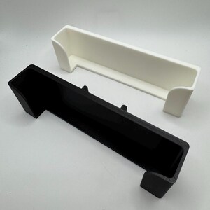 Puede incluir: Dos contenedores de almacenamiento rectangulares, uno negro y otro blanco, se muestran sobre un fondo blanco. Cada contenedor tiene una parte superior larga y abierta y dos lados cortos e inclinados, lo que sugiere un dise&ntilde;o tipo bandeja. Los contenedores son de material s&oacute;lido.
