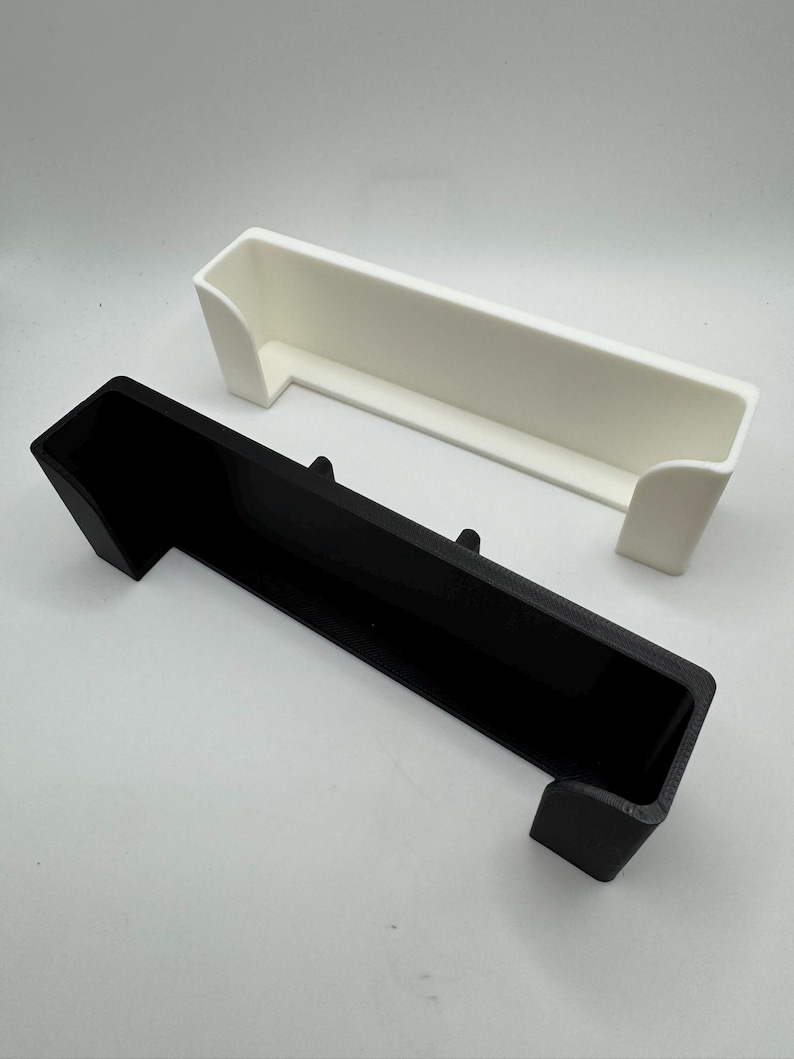 Puede incluir: Dos contenedores de almacenamiento rectangulares, uno negro y otro blanco, se muestran sobre un fondo blanco. Cada contenedor tiene una parte superior larga y abierta y dos lados cortos e inclinados, lo que sugiere un dise&ntilde;o tipo bandeja. Los contenedores son de material s&oacute;lido.