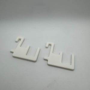 May include: Two white plastic shelf supports with a hook and a rectangular base. The supports are designed to hold shelves in place. The supports are made of a solid, opaque white plastic.