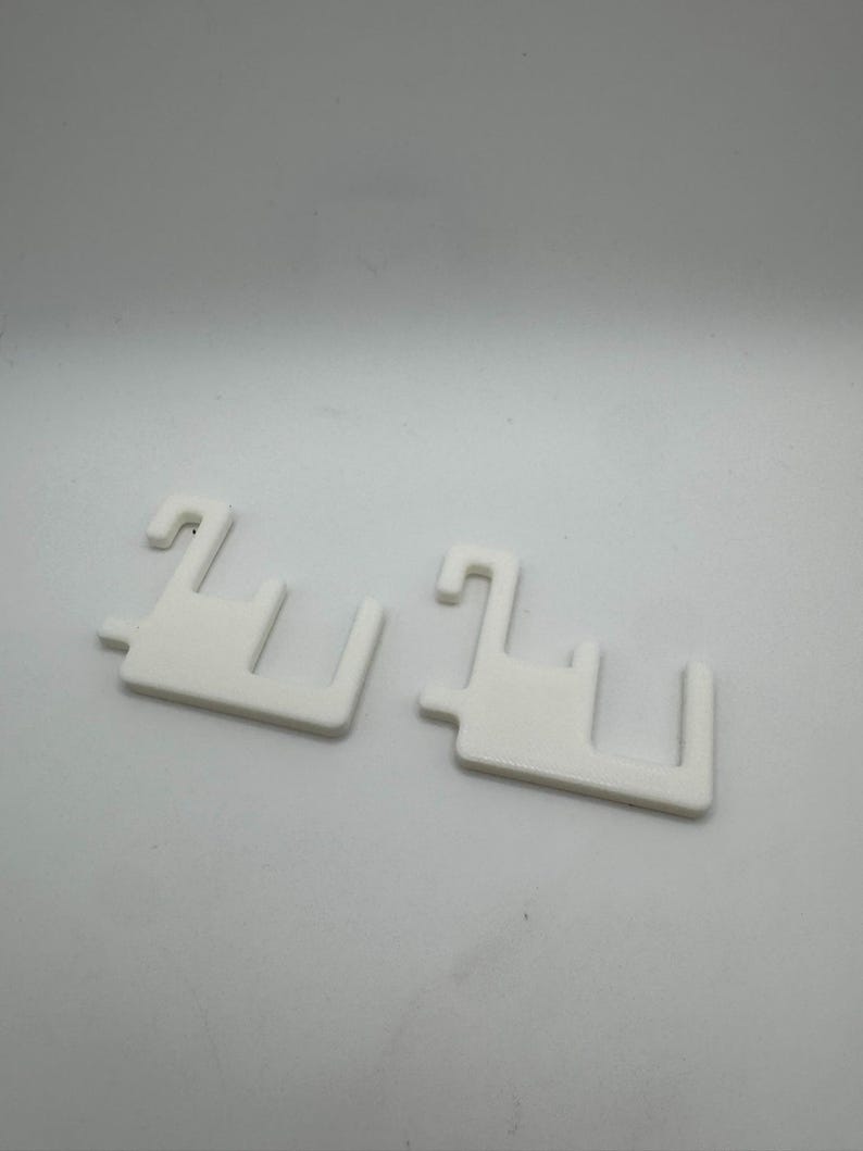 May include: Two white plastic shelf supports with a hook and a rectangular base. The supports are designed to hold shelves in place. The supports are made of a solid, opaque white plastic.