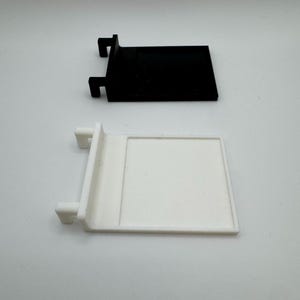 May include: Two plastic shelf brackets, one black and one white. The brackets have a rectangular shape with a small lip on the top and two small tabs on the side.