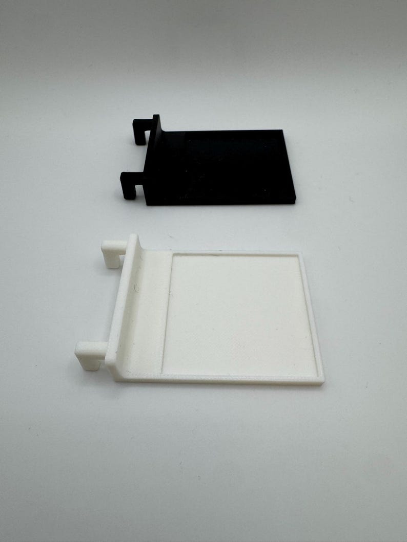 May include: Two plastic shelf brackets, one black and one white. The brackets have a rectangular shape with a small lip on the top and two small tabs on the side.