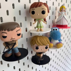 Op de afbeelding: Vier popcultuurfiguren die op een wit prikbord worden getoond. De figuren zijn een meisje met bruin haar in een groene jurk, een man met bruin haar en een baard die een boog en pijl vasthoudt, een blonde jongen met een zwaard en een blauw en wit gehaakt figuur.