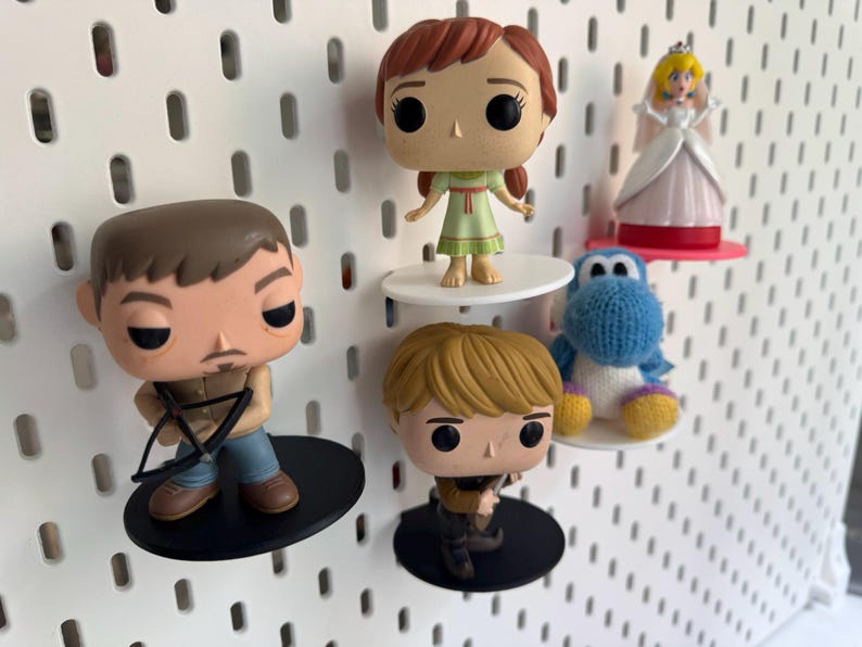 Op de afbeelding: Vier popcultuurfiguren die op een wit prikbord worden getoond. De figuren zijn een meisje met bruin haar in een groene jurk, een man met bruin haar en een baard die een boog en pijl vasthoudt, een blonde jongen met een zwaard en een blauw en wit gehaakt figuur.
