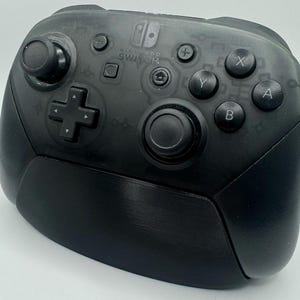 Op de afbeelding: Een zwarte Nintendo Switch Pro Controller. De controller heeft een D-pad, analoge sticks en actieknoppen met de labels X, Y, A en B. Het Nintendo Switch-logo is zichtbaar in het midden bovenaan.