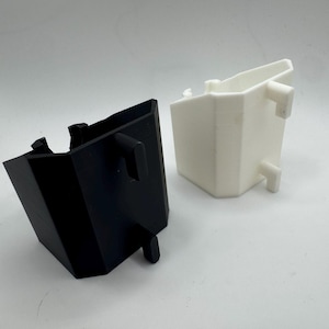 May include: Two plastic, geometric-shaped containers. One is black, the other is white. Both have a similar design with a rectangular body and protruding tabs. The containers are likely components of a larger product or system.