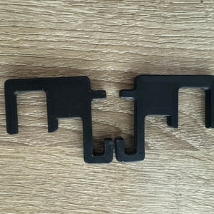 May include: Two black plastic hooks with a square opening in the middle. The hooks are connected at the bottom.