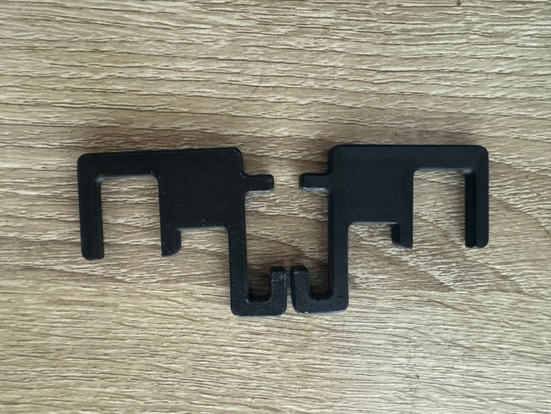May include: Two black plastic hooks with a square opening in the middle. The hooks are connected at the bottom.