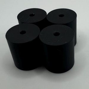 May include: Four black cylindrical objects with a hole in the center. The objects are arranged in a square pattern.