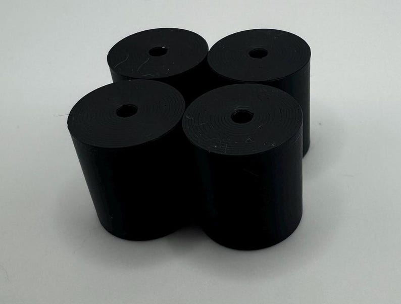 May include: Four black cylindrical objects with a hole in the center. The objects are arranged in a square pattern.