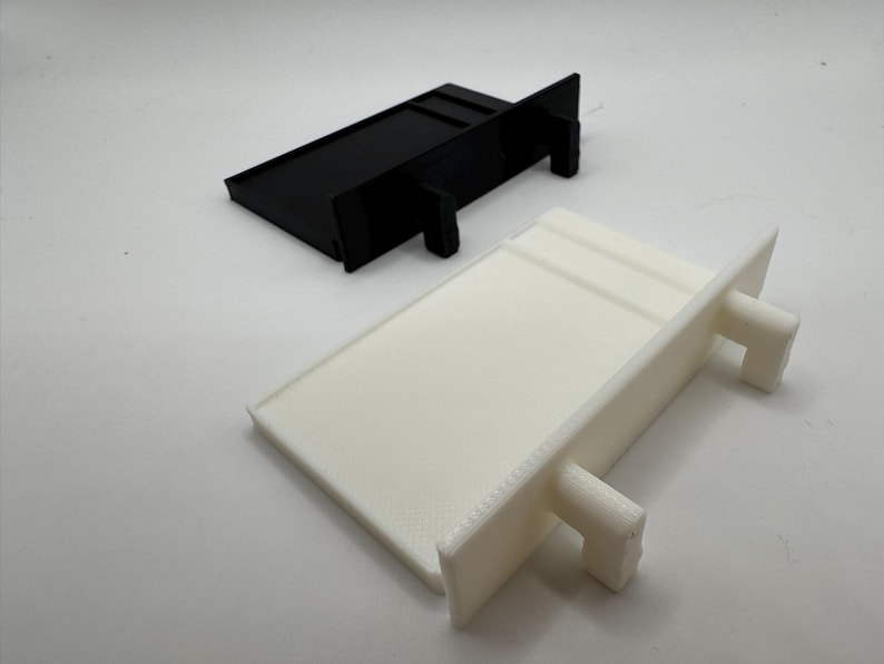 May include: Two plastic shelf brackets, one black and one white. The brackets are rectangular in shape with two small tabs on the side.