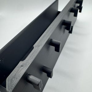 Peut inclure: Un organisateur rectangulaire noir avec un bord textur&eacute; et plusieurs crochets carr&eacute;s saillants. L'organisateur a un canal profond et est con&ccedil;u pour contenir des objets. L'objet est fait d'un mat&eacute;riau noir mat.