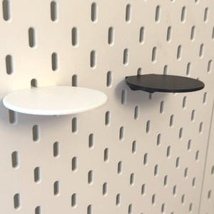 Op de afbeelding: Twee ronde pegboard-planken, een zwarte en een witte, gemonteerd op een witte pegboard-wand.