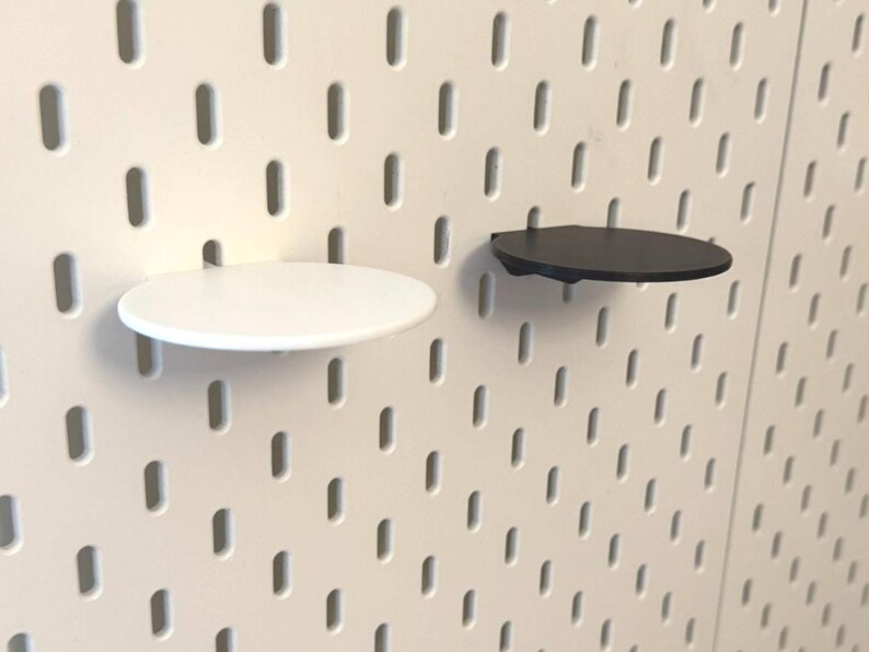 Op de afbeelding: Twee ronde pegboard-planken, een zwarte en een witte, gemonteerd op een witte pegboard-wand.