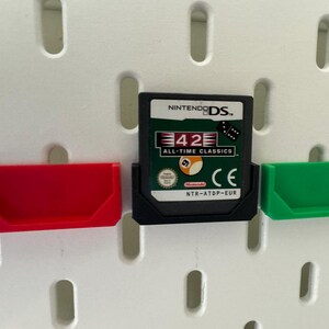 May include: A black Nintendo DS game cartridge with a white label. The label features the text "42 All-Time Classics" and a picture of a billiard ball. The cartridge is in a clear plastic case with a green and red plastic holder.