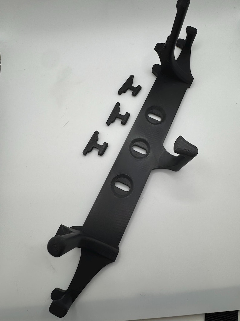 May include: A black plastic stand with a long, rectangular body and three oval-shaped holes. The stand has two curved arms at the top and two legs at the bottom. Three small, black, H-shaped pieces are also included.