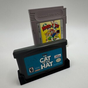 May include: Two video game cartridges. One is gray with "Nintendo GAME BOY" printed on it, and a colorful label that says "Mario's Picross". The other is black with "THE CAT IN THE HAT" printed on a blue label.