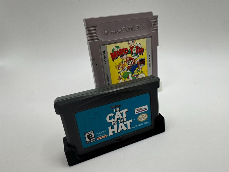 May include: Two video game cartridges. One is gray with "Nintendo GAME BOY" printed on it, and a colorful label that says "Mario's Picross". The other is black with "THE CAT IN THE HAT" printed on a blue label.