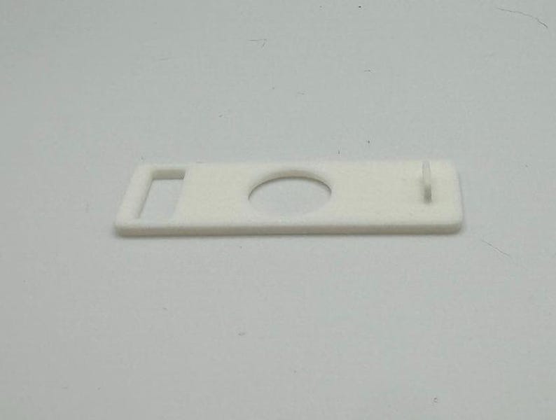 Pu&ograve; includere: Pezzo di plastica bianco con un foro rotondo e una piccola apertura rettangolare.