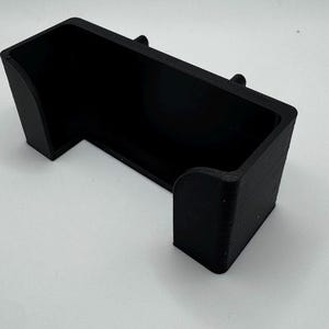 Pu&ograve; includere: Un supporto per telefono in plastica nera con un design curvo. Il supporto &egrave; progettato per tenere un telefono in posizione verticale.