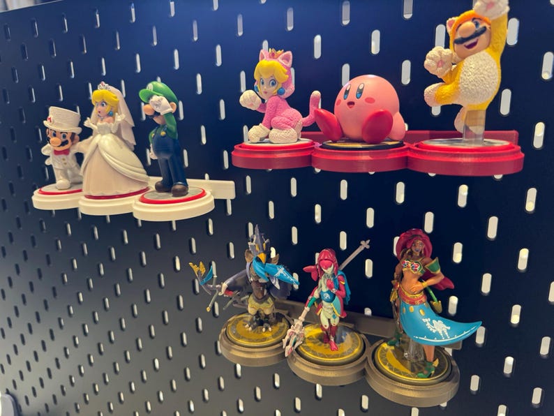 May include: A collection of colorful Nintendo character figurines displayed on a black pegboard wall. The figurines include Mario, Luigi, Peach, Toad, Link, Zelda, and Kirby.