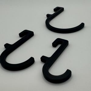 Puede incluir: Tres ganchos de pl&aacute;stico negro en forma de J. Los ganchos est&aacute;n dise&ntilde;ados para colgar objetos en una pared u otra superficie.
