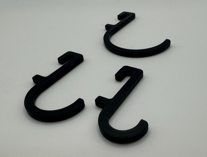 Puede incluir: Tres ganchos de pl&aacute;stico negro en forma de J. Los ganchos est&aacute;n dise&ntilde;ados para colgar objetos en una pared u otra superficie.