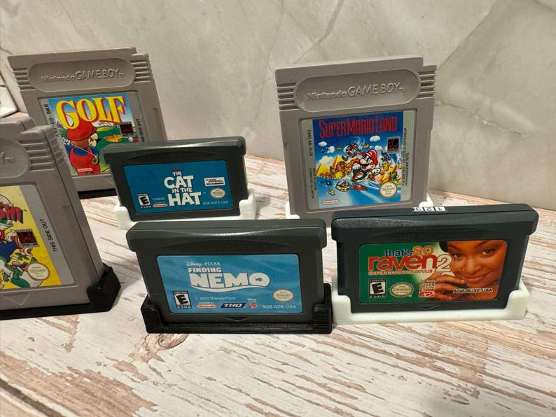 May include: A collection of retro video game cartridges, including titles like "Golf," "Super Mario Land," "Finding Nemo," and "That's So Raven 2." The cartridges are in various colors and designs, with labels featuring game titles and artwork.