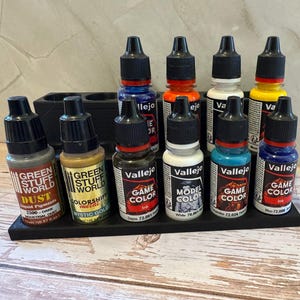 Puede incluir: Un organizador negro contiene varios botes de pintura con tapas negras y contenidos coloridos. Los botes est&aacute;n etiquetados con marcas como Vallejo y Green Stuff World, e incluyen colores como rojo, azul, amarillo y blanco. Los botes est&aacute;n colocados en una bandeja negra.