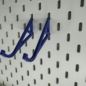 May include: Two blue plastic wall mounted hooks for hanging items on a pegboard.