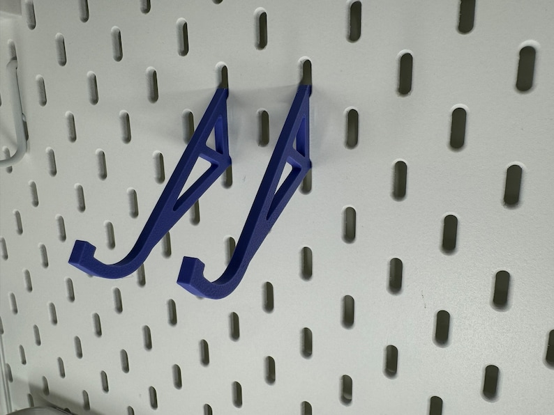 May include: Two blue plastic wall mounted hooks for hanging items on a pegboard.