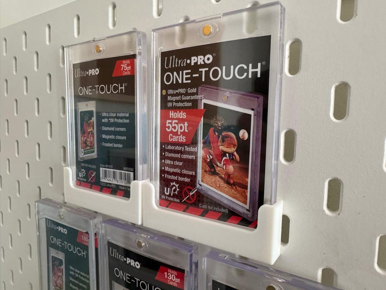 May include: Clear Ultra PRO ONE-TOUCH card holders, designed to protect trading cards. The holders are displayed on a white pegboard. The labels indicate the holders can hold 55pt, 75pt, and 130pt cards. Features include UV protection and magnetic closure.