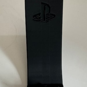 May include: A black plastic stand with a PlayStation logo for holding a video game controller.