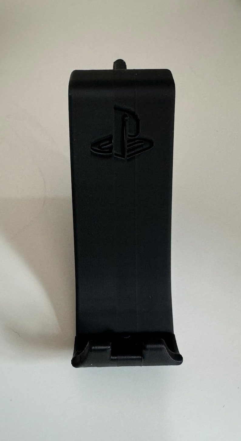 May include: A black plastic stand with a PlayStation logo for holding a video game controller.