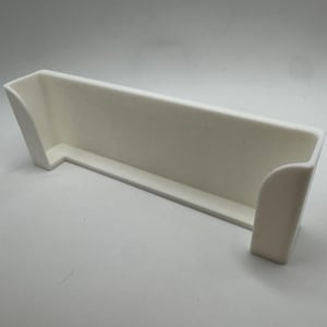 Pu&ograve; includere: Un contenitore bianco rettangolare con la parte superiore aperta, un bordo curvo su un lato e lati angolati. Realizzato in materiale opaco, poggia su una superficie bianca. Il design &egrave; semplice e moderno.