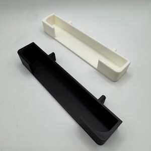 May include: Two rectangular, open-top containers. One is black, the other is white. Both have a rectangular shape with a small, raised tab on the side. The containers are likely 3D-printed.
