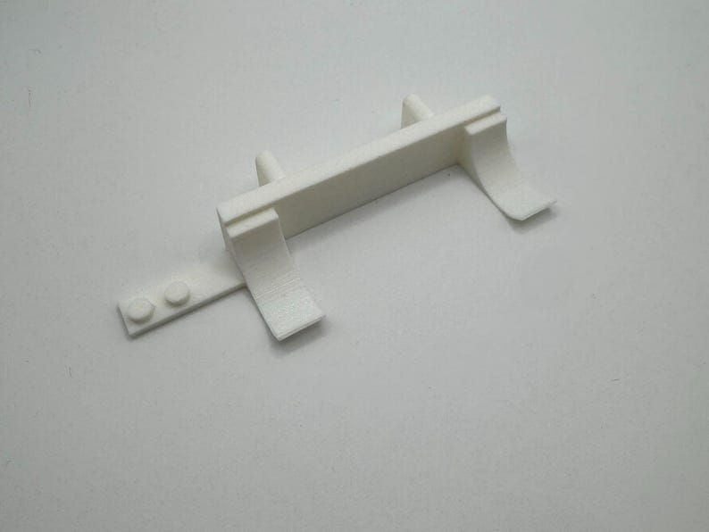 May include: White plastic model of a truck bed with a raised platform and two side rails. The bed has a small, rectangular piece attached to the back.