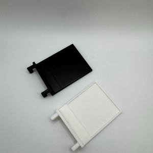 May include: Two plastic wall mounts, one black and one white. Each mount has a rectangular shape with a small lip on the top and two small tabs on the bottom.
