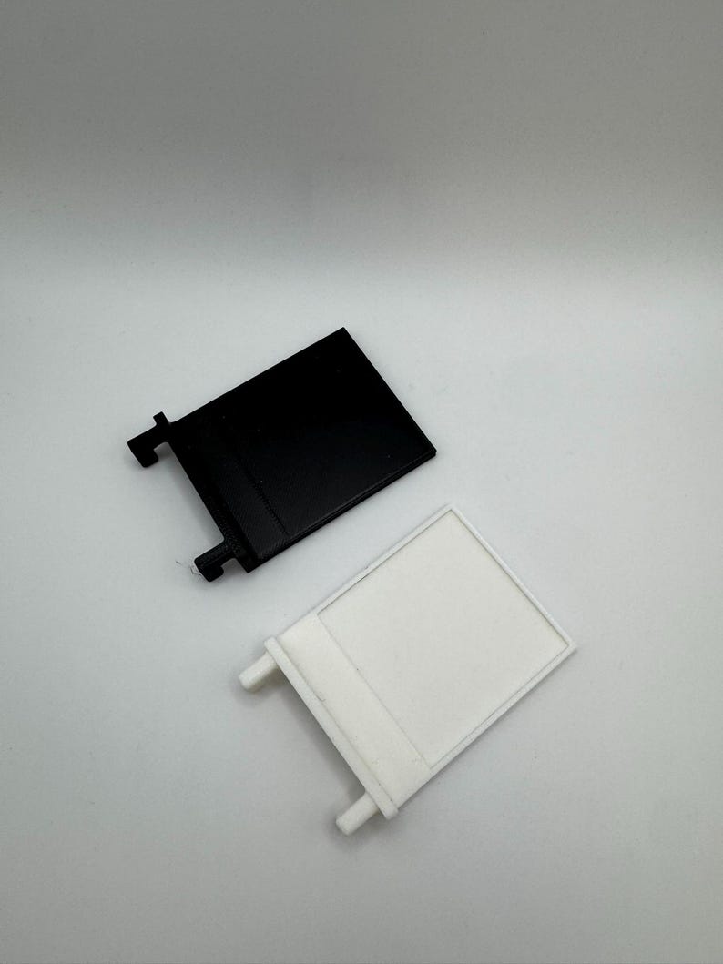 May include: Two plastic wall mounts, one black and one white. Each mount has a rectangular shape with a small lip on the top and two small tabs on the bottom.