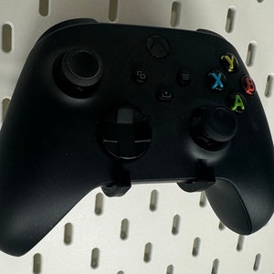 May include: A black Xbox Series X controller with a black and white D-pad, black buttons, and green, yellow, and red face buttons.