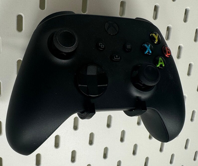 May include: A black Xbox Series X controller with a black and white D-pad, black buttons, and green, yellow, and red face buttons.