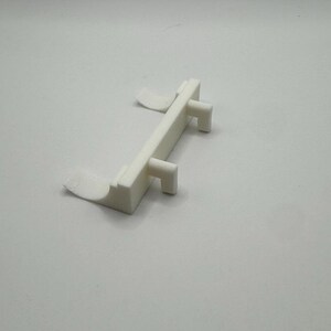 Op de afbeelding: Witte plastic deurstop met twee lipjes aan de zijkant en twee lipjes aan de bovenkant.