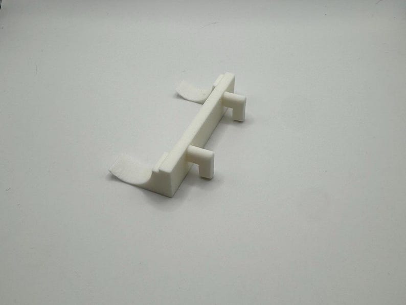 Op de afbeelding: Witte plastic deurstop met twee lipjes aan de zijkant en twee lipjes aan de bovenkant.