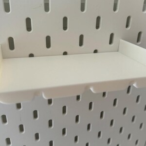 May include: White plastic shelf with a curved front edge, designed to be mounted on a pegboard wall.