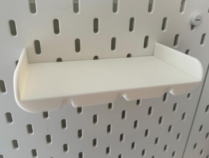 May include: White plastic shelf with a curved front edge, designed to be mounted on a pegboard wall.