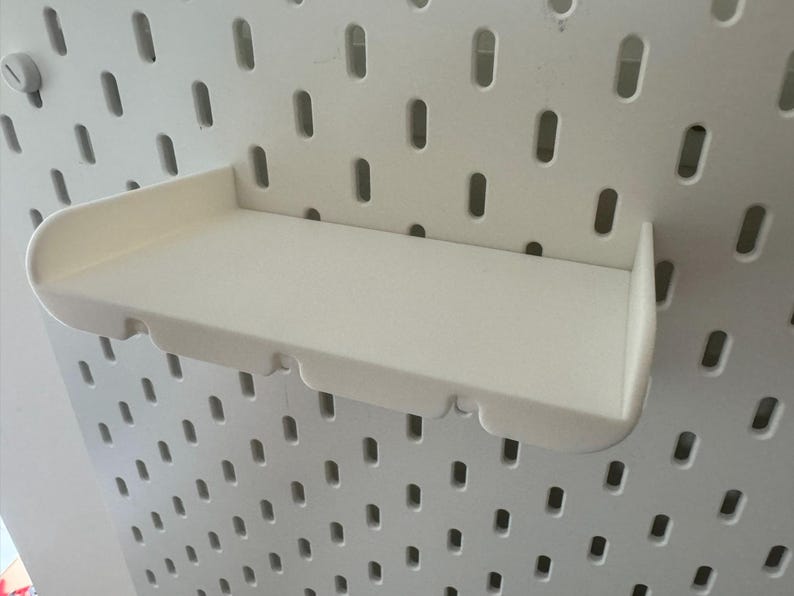 May include: White plastic shelf with a curved front edge, designed to hang on a pegboard wall.