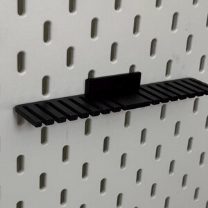 K&ouml;nnte beinhalten: Schwarzer Kunststoff-Pegboard-Organizer mit 16 Steckpl&auml;tzen zum Aufbewahren von Werkzeugen oder anderen kleinen Gegenst&auml;nden.
