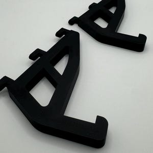 May include: Two black plastic shelf brackets with a grid pattern. The brackets are designed to support shelves.